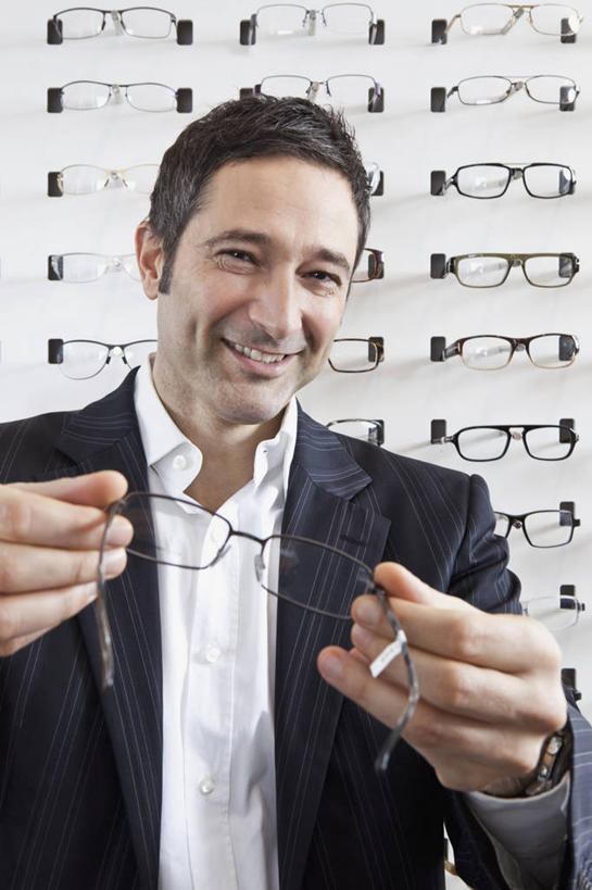 西方人,一个人,商店,站,笑,微笑,露齿笑,竖图,室内,白天,正面,西装,欧洲,欧洲人,仅一个男性,仅一个人,仅一个中年男性,握,套装,正装,眼镜,拿,拿着,注视,职业装,商铺,货架,架子,观察,看,站着,握着,观看,验光师,察看,关注,陈列架,近视眼镜,眼镜店,超市货架,市肆,商号,男人,男性,中年男性,白种人,站立,半身,彩图,店铺