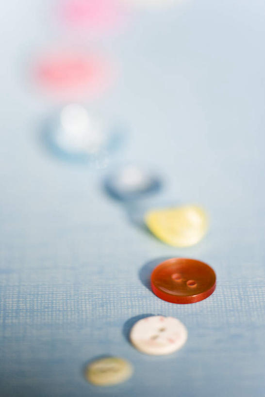 无人,竖图,俯视,室内,特写,白天,桌面,桌子,静物,一排,许多,阴影,朦胧,模糊,弯曲,整齐,光线,影子,纽扣,扣子,排列,黄色,红色,蓝色,白色,阳光,队列,彩图,高角度拍摄