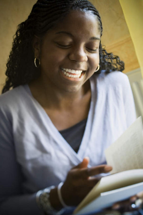 西方人,一个人,笑,微笑,露齿笑,竖图,室内,白天,仰视,看书,阅读,书籍,欧洲,非洲,黑人,欧洲人,仅一个年轻女性,仅一个女性,仅一个人,握,学习,服装,拿,拿着,注视,休闲装,装饰品,衣服,耳环,饰品,手链,首饰,书本,观察,看,休闲,休闲服,读书,浏览,握着,服饰,手镯,观看,察看,关注,镯子,耳饰,年轻女性,女人,女性,非洲人,书,图书,半身,彩图,低角度拍摄