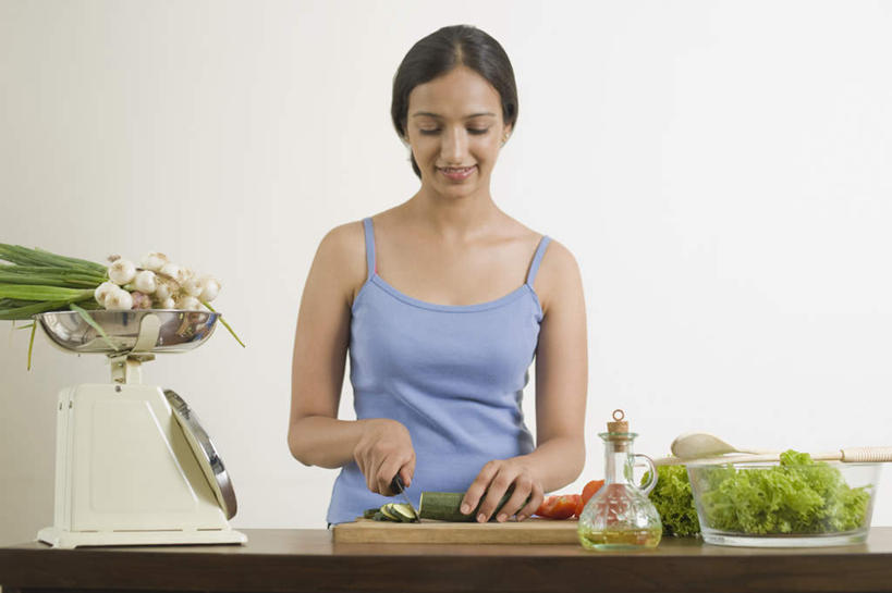 一个人,站,笑,微笑,露齿笑,横图,室内,白天,正面,仪器,餐桌,桌子,黄瓜,蔬菜,蒜,西红柿,金属制品,亚洲,仅一个年轻女性,仅一个女性,仅一个人,服装,新鲜,金属,工具,食品,案板,刀具,电子秤,拿,拿着,注视,休闲装,砧板,食物,衣服,刀,观察,看,切,站着,休闲,休闲服,服饰,有机食品,绿色食品,餐台,观看,察看,衡量,关注,菜刀,计量,衡器,切菜刀,年轻女性,女人,女性,亚洲人,印度人,秤,小蒜,青瓜,胡瓜,番茄,大蒜,站立,半身,彩图,电子称