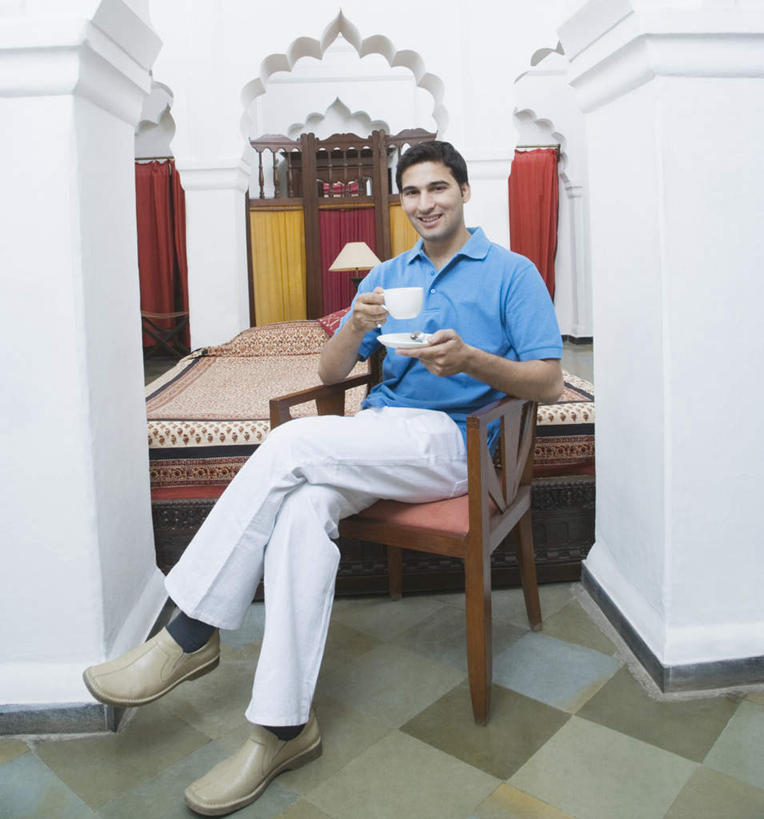 一个人,坐,笑,微笑,露齿笑,竖图,室内,白天,正面,床,卧室,杯子,椅子,亚洲,仅一个男性,仅一个人,服装,瓷器,瓷砖,地砖,双人床,灯光,床单,咖啡杯,陶瓷制品,地面,拿,拿着,注视,休闲装,被子,灯,仅一个年轻男性,衣服,灯具,观察,看,休闲,休闲服,服饰,观看,察看,被单,照明设备,关注,床头灯,瓷杯,男人,男性,年轻男性,亚洲人,印度人,坐着,彩图,全身,睡房,卧房