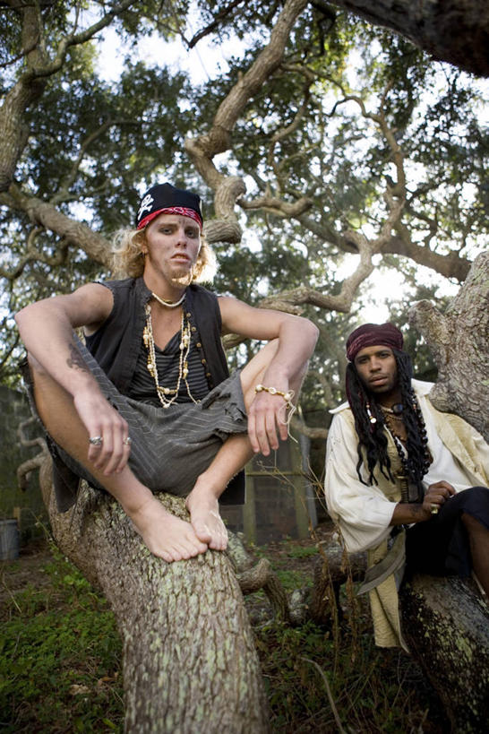 西方人,两个人,伙伴,朋友,坐,竖图,室外,白天,正面,友谊,草地,草坪,植物,项链,欧洲,非洲,黑人,欧洲人,阴影,服装,光线,头巾,影子,注视,装饰品,草,树,树木,衣服,绿色,天空,阳光,自然,饰品,首饰,天,观察,看,搭,海盗,服饰,生长,成长,观看,察看,衣着,穿着,搭着,关注,表演服,演出服,衣饰,道具服,友情,男人,男性,年轻男性,白种人,非洲人,坐着,半身,彩图