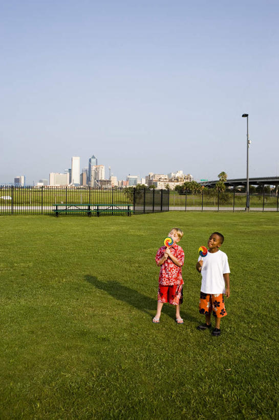 西方人,儿童,两个人,伙伴,朋友,高楼大厦,栏杆,站,吃,竖图,室外,白天,正面,友谊,纯洁,办公楼,草地,草坪,植物,大厦,建筑,路灯,摩天大楼,写字楼,照明,欧洲,非洲,黑人,欧洲人,握,阴影,服装,光线,棒棒糖,影子,围栏,灯光,食品,糖,糖果,甜点,甜品,拿,拿着,注视,休闲装,护栏,灯,草,树,树木,食物,小孩,衣服,蓝色,绿色,蓝天,天空,阳光,自然,楼宇,甜食,天,观察,看,站着,休闲,休闲服,商务楼,可爱,童年,童趣,握着,服饰,生长,晴朗,成长,观看,照亮,察看,照明设备,关注,童真,烂漫,无邪,波板糖,万里无云,天真,友情,男孩,男人,男性,白种人,非洲人,晴空,晴空万里,嚼,食,站立,彩图,全身,大楼,高层建筑,高楼,摩天楼,男生