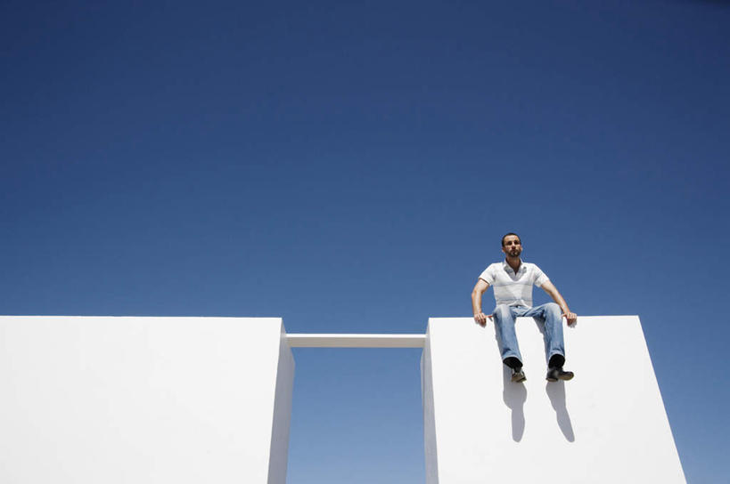 西方人,一个人,坐,竖图,室外,白天,仰视,欧洲,欧洲人,仅一个男性,仅一个人,服装,墙,缺口,注视,休闲装,墙壁,墙面,仅一个年轻男性,衣服,蓝色,白色,蓝天,天空,天,低头,观察,看,休闲,思考,休闲服,服饰,晴朗,观看,察看,关注,独木桥,底座,万里无云,思虑,垂头,男人,男性,年轻男性,白种人,晴空,晴空万里,坐着,彩图,低角度拍摄,全身