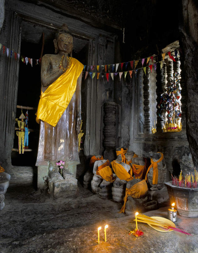 无人,寺庙,竖图,室内,白天,正面,旅游,度假,石头,名胜古迹,门,标志建筑,地标,建筑,旗帜,蜡烛,雕塑,柬埔寨,亚洲,阴影,节日,遗迹,艺术,装饰,光线,雕刻,雕像,火焰,石子,影子,烛光,墙,烟雾,燃烧,古迹,文化,文物,娱乐,旗子,建设,古建筑,经幡,墙壁,墙面,佛香,香火,香烛,工艺品,门框,庙宇,点燃,祈祷,享受,休闲,健康,旅游胜地,放松,许愿,宗教,东南亚,信仰,烧香,纪念,祈求,美术,主题,陈列,古文明,沉积岩,风马旗,暹粒,高棉,柬埔寨王国,功能,美学,旌旗,旗号,吉蔑,水成岩,平安,石块,岩石,彩图,庙,寺