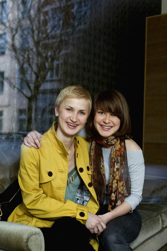 西方人,两个人,伙伴,朋友,家,坐,握手,笑,微笑,露齿笑,竖图,室内,白天,正面,友谊,植物,窗户,落地窗,沙发,欧洲,欧洲人,服装,裤子,装饰,房屋,屋子,牛仔裤,休闲装,楼房,玻璃窗,住宅,树,树木,衣服,绿色,自然,围巾,休闲,温暖,休闲服,服饰,生长,成长,围脖,保暖,华丽,点缀,夹克,御寒,布艺沙发,衬托,美观,雅致,雅观,茄克,友情,年轻女性,女人,女性,白种人,搀手,拉手,手搀手,手拉手,手牵手,手握手,坐着,半身,彩图,房子