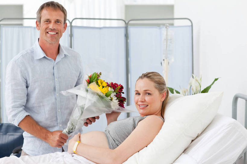 西方人,中年人,孕妇,两个人,家庭,夫妻,医院,站,躺,笑,微笑,露齿笑,横图,室内,白天,正面,爱情,床,家具,靠垫,屏风,吊带,欧洲,欧洲人,握,服装,盛开,包装,包装纸,纸,床单,靠枕,纸张,浪漫,拿,花蕾,拿着,扭头,注视,吊带衫,被子,花,花瓣,花朵,鲜花,衣服,病床,垫子,枕头,花苞,花蕊,观察,看,站着,转头,温暖,温馨,一家人,怀孕,恩爱,握着,恋人,服饰,观看,协调,和睦,察看,包装材料,被单,遮挡,待产,衣着,穿着,关注,分隔,医疗机构,妊娠,准妈妈,衣饰,美化,露脐装,卧着,男人,男性,女人,女性,中年男性,中年女性,白种人,夫妇,情侣,产妇,躺着,卧,站立,半身,彩图,病院,诊所,护理床,医疗床,玻璃纸,伴侣,融洽